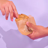 Raspberry White Chocolate New York Cookie being shared, freshly baked by Crumbs & Doilies in brown branded paper.